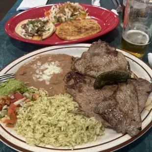 Carne asada plate and taco and pupusa in background.