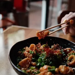 a person holding chopsticks over a bowl of food