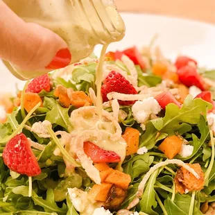 a person pouring dressing on a salad