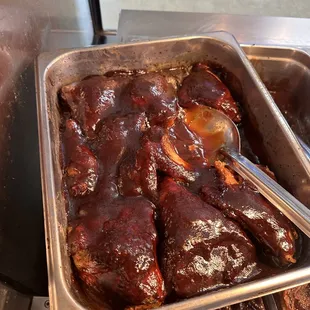 a tray of ribs with sauce and a spoon