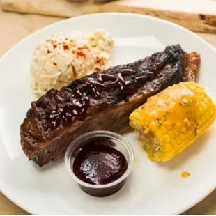 a plate of ribs, corn and barbecue sauce