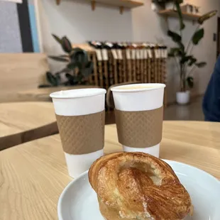 a croissant on a plate with two cups of coffee