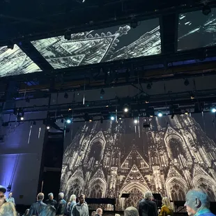 people sitting at tables in front of a projection of a cathedral