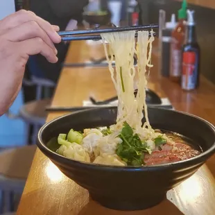 a person holding chopsticks over a bowl of noodles