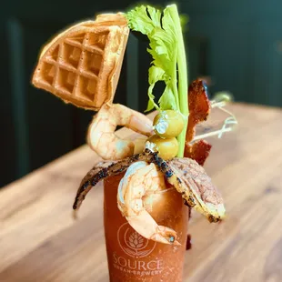 a bloody drink with shrimp, bacon, and waffles