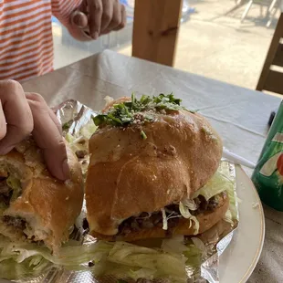 Torta with carne asada, loaded with lettuce, tomatoes, avocado and melted cheese over top.