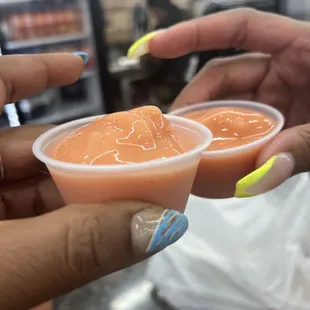 a person holding two cups of sauce