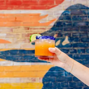 a person holding a drink in front of a brick wall