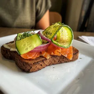 Salmon Toast $9.25 *Smoked Salmon, Herb Cream Cheese, Thin Sliced Onion, Cucumber Ribbons, and Dill on toasted Pumpernickel.