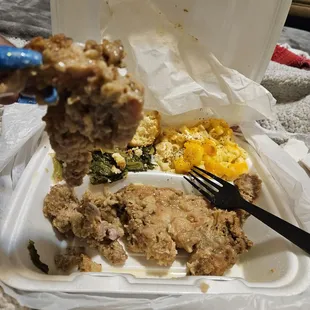 a fork picking up a piece of fried chicken from a styrofoam container