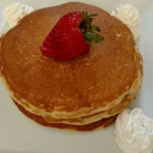 a stack of pancakes with whipped cream and a strawberry on top