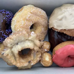 Chocolate cake with purple sprinkles. Maple  old fashioned filled deep fried upper right. Strawberry  glazed cake.