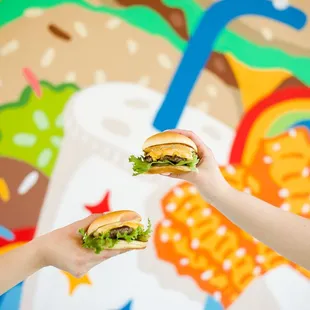 two people holding sandwiches in front of a mural