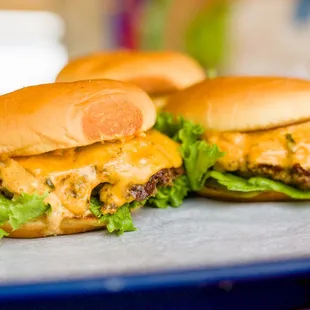 two hamburgers with cheese and lettuce on a tray