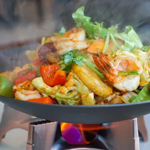 a wok with shrimp and vegetables cooking over a fire