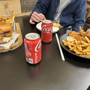 a man sitting at a table with a plate of fried chicken and a can of coke