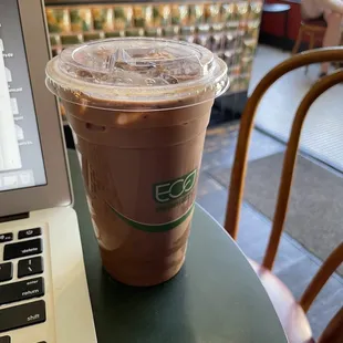 a cup of iced coffee on a table with a laptop