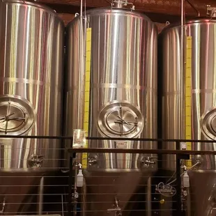 a woman standing in front of a row of stainless steel tanks