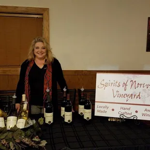 a woman standing in front of a table with bottles of wine