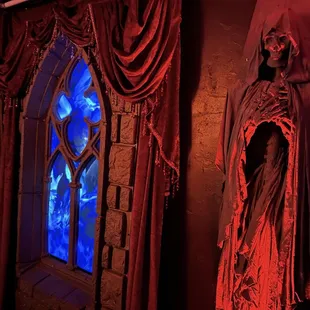 a skeleton dressed in a robe and cloak in front of a stained glass window