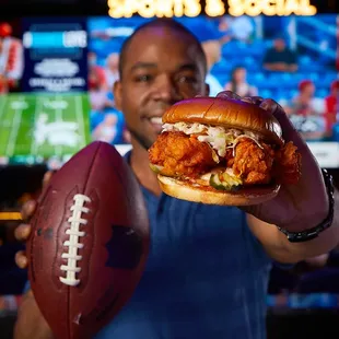 a man holding a football and a chicken sandwich