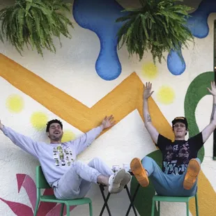 two men sitting on chairs in front of a mural
