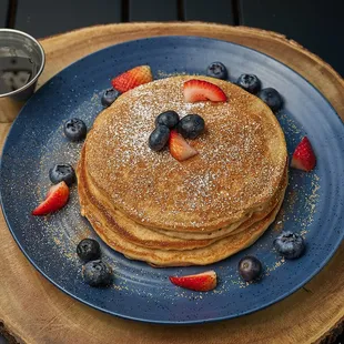 Three fluffy pancakes with cinnamon sugar dust. Served with fresh fruit, mint, and chocolate sauce with syrup.