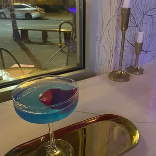 a blue cocktail in a glass on a tray