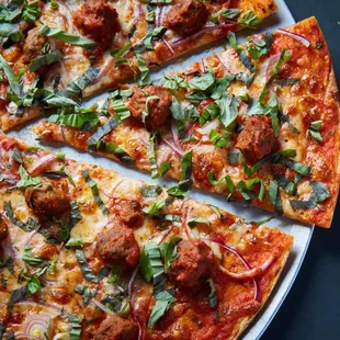 a sliced pizza with meatballs and herbs