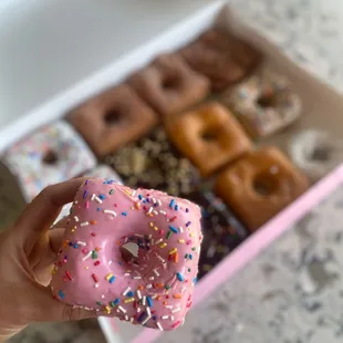 a hand holding a pink donut with sprinkles