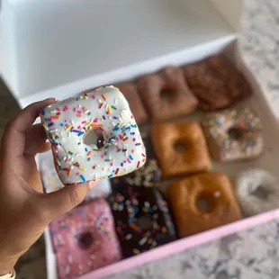 a hand holding a square donut with sprinkles