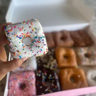 a hand holding a square donut with sprinkles
