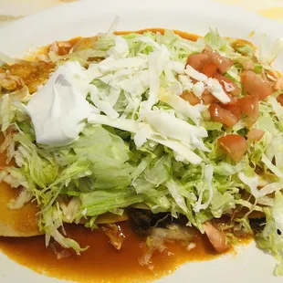 Enchiladas Supremas with shredded lettuce, diced tomatoes, and sour cream on top