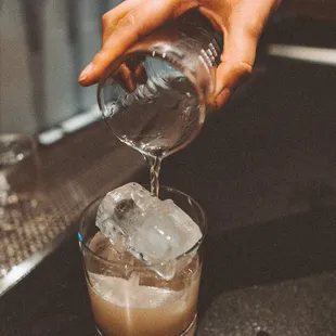 a person pouring a drink into a glass