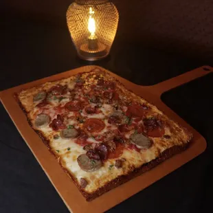 a square pizza on a cutting board with a lit candle in the background