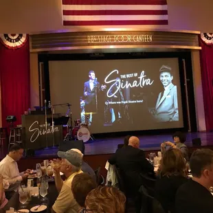 people sitting at tables in front of a screen