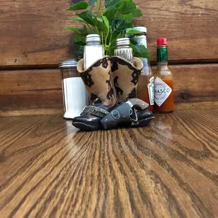a cowboy boot, a bottle of hot sauce, and a pair of shoes on a table