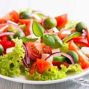 a plate of salad with tomatoes, lettuce and olives