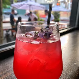 a glass of red drink with a purple flower garnish