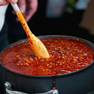 a person stirring a pot of chili