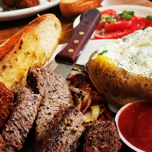 a plate of meat, bread, and a baked potato