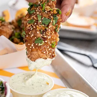 a hand dipping a piece of fried chicken