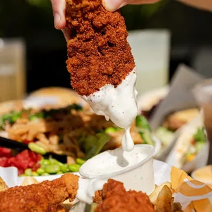 a hand dipping a piece of fried chicken