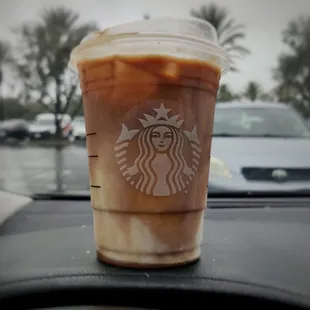a cup of iced coffee on the dashboard of a car