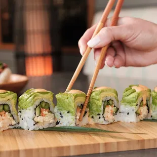 a person holding chopsticks over a sushi roll