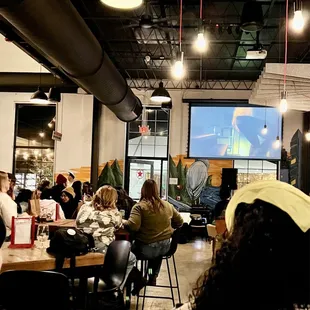 people sitting at tables and watching a screen