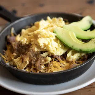 a skillet of food with eggs and avocado