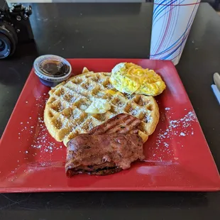 a plate of waffles, bacon and eggs