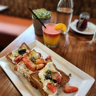 a plate of toast with strawberries, blueberries, and orange juice