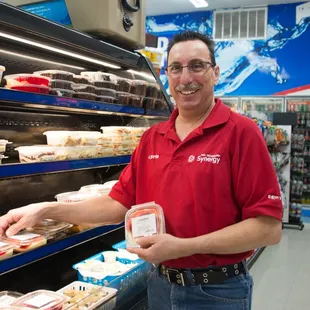 a man in a red shirt standing in front of a display of cheeses